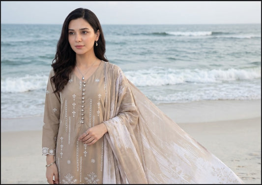 Woman in a beige traditional outfit standing on a beach with ocean waves in the background